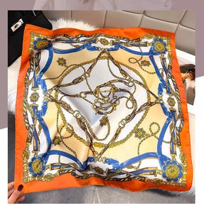 Detail of luxury silk scarf with chain print and orange border on plush background