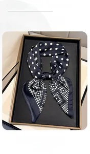 Close-up of black satin neckerchief with white polka dots in a golden luxury display box