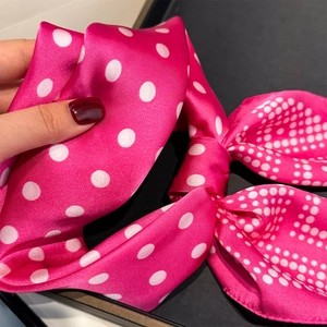 Close-up of a magenta satin scarf with white polka dots held by hand to show texture