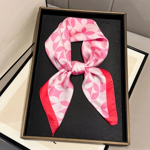 Detailed close-up of pink geometric silk scarf with red stitching in a premium black box