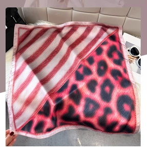 Close-up of leopard and stripe pattern silk scarf with red stitched edges on a white fur mat