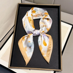 Elegant floral silk scarf in beige with orange accents displayed on a black tray