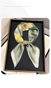 Dettaglio di un foulard in seta floreale verde erba con bordo bianco sul vassoio