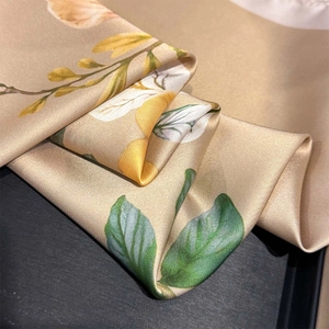 Dettaglio di un foulard in seta oro champagne con texture satinata e motivi floreali