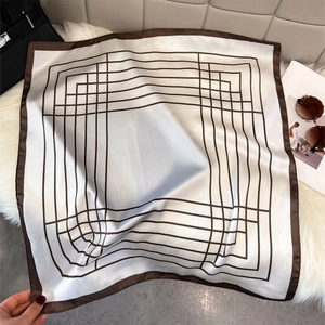 Flat lay of a 70cm geometric silk scarf styled with a luxury bag and sunglasses