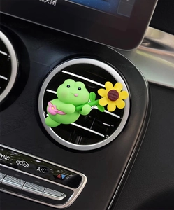 Close-up of a cute green frog car vent clip with sunflower on a black interior dashboard