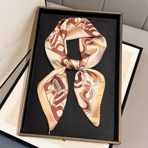 Champagne silk scarf with geometric chain prints on a bronze tray in soft lighting