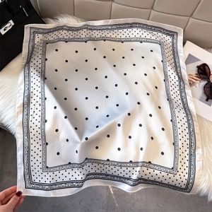 Classic black and white polka dot silk scarf displayed with a luxury handbag and magazine