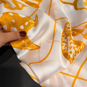 Macro shot of soft satin square scarf featuring vibrant orange floral shell prints