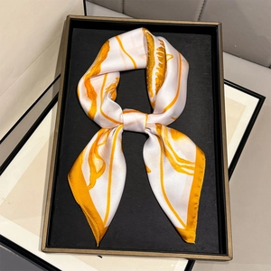 Elegant white silk scarf with yellow abstract shell print displayed on a black golden tray