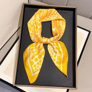 Dettaglio di un foulard in seta a pois gialli annodato a fiocco su un vassoio nero
