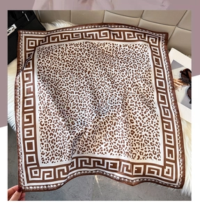 Flat lay of a leopard print satin square scarf with greek key patterns on soft plush background