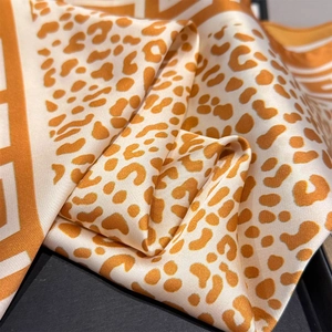Detailed close-up of glossy leopard print silk scarf in vibrant orange and ivory
