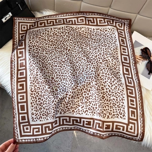 Leopard print silk square scarf with Greek key pattern border on white plush rug