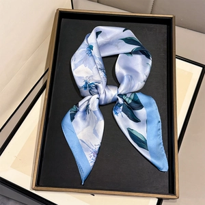 Detail of light blue silk scarf with white camellia floral pattern on a black tray