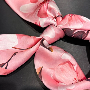 Detailed close-up of pink camellia floral print silk scarf tied in a decorative knot