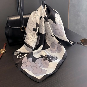 Elegant camellia print silk square scarf tied on a luxury black handbag in a city setting