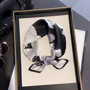 Elegant camellia print silk scarf tied in a bow on a black tray with luxury accessories