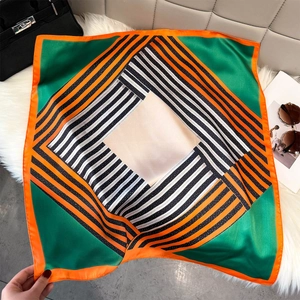 Flat lay of a silk square scarf with orange borders and green geometric stripe patterns