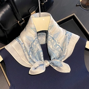 Detail of silk paisley square scarf styled on a navy knit vest with premium accessories