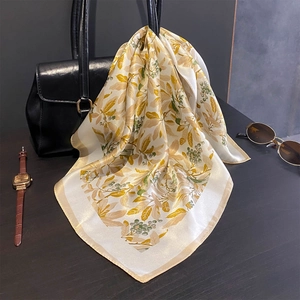 Silk square scarf with yellow leaf print hanging on a black handbag in a lifestyle setting
