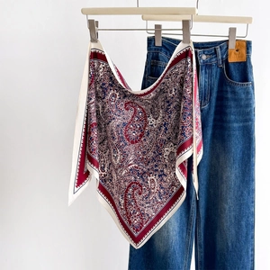 Vintage paisley silk scarf in burgundy and navy hanging on a wooden hanger with jeans