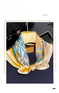 Détail d'un carré de soie aux motifs jaunes et bleus noué élégamment sur un sac à main