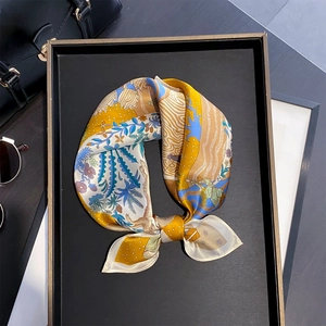 Carré de soie artistique avec imprimés floraux posé sur un sac à main et un plateau