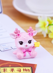 Nahaufnahme einer rosa Hirschfigur aus Harz mit Geschenkbox auf einem Laptop-Schreibtisch