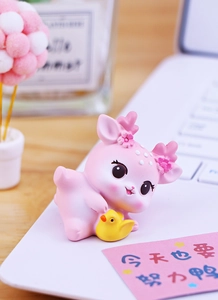 Süße rosa Hirschfigur mit gelber Ente auf Schreibtisch neben einem Laptop