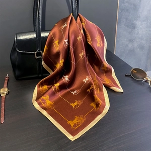 Detail of luxury silk scarf with horse carriage print draped over a black leather bag