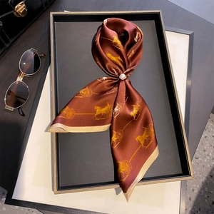 Detail of silk scarf with golden carriage print and elegant pearl ring buckle on a tray