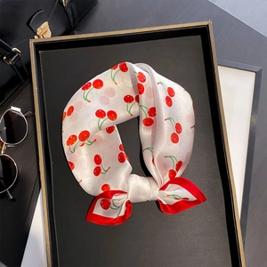 Silk scarf with red cherry print and contrast border shown in a luxury flat lay