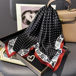 Polka dot silk scarf with red paisley border draped on a brown leather luxury handbag