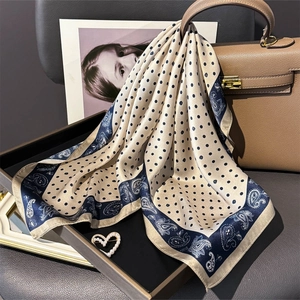 Silk scarf with blue polka dots and paisley print draped over a luxury leather handbag