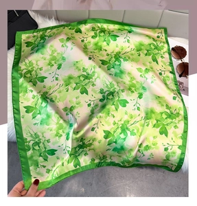 Detailed close-up of green botanical print silk scarf on a soft white plush surface