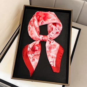 Elegant square silk scarf with floral print and red borders displayed on a black tray