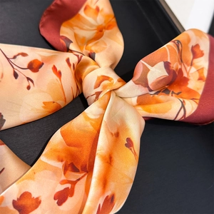 Detailed view of the vibrant floral print and silky texture of this orange scarf