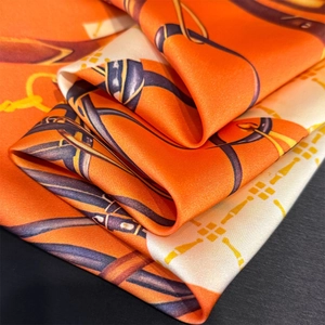 Macro detail of the chain and equestrian print on a luxury orange silk square scarf
