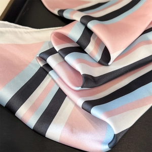 Detailed close-up of striped silk scarf texture with pink and blue geometric pattern