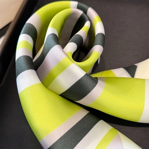 Macro detail of geometric striped silk scarf featuring vibrant green and purple tones