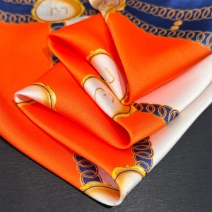 Detailed close-up of silk square scarf showing orange and blue patterns with gold chain motifs