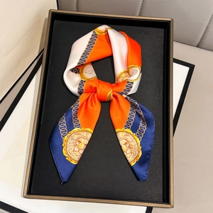 Close-up of silk-textured bow scarf with lion emblem and chain print on a display tray