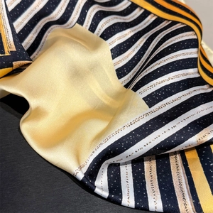 Close-up of geometric striped silk scarf showing silky texture and elegant yellow accents