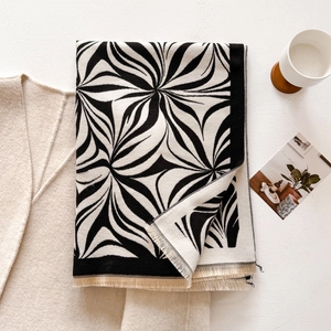 Detail of soft winter scarf with black wave patterns and beige tassels on a white table