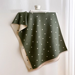 Detail of dark green cashmere-feel scarf with white heart patterns and soft fringe edges
