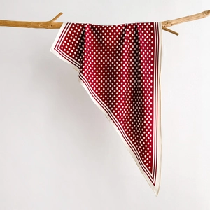 Detail of dark red polka dot silk scarf draped elegantly on a natural wooden branch