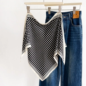 Classic black and white polka dot silk scarf with striped edges shown against a white wall