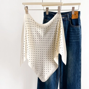 Elegant polka dot silk scarf in beige and black draped with denim pants on a hanger