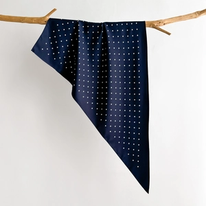 Close-up of navy blue polka dot silk scarf draped elegantly over a natural wood branch